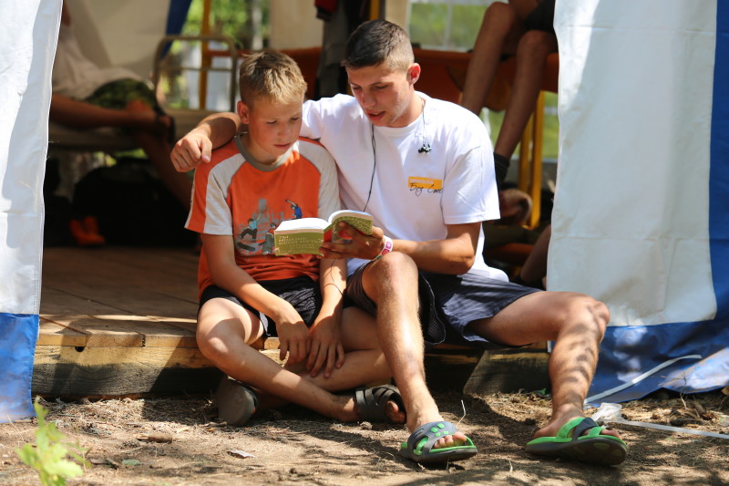 School Without Walls leader reading the New Testament with a child at summer Bible camp
