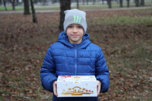 Ukrainian boy in a park holding an open Gift of Hope Ukraine box filled with sweets and a colorful Christian Scripture book.