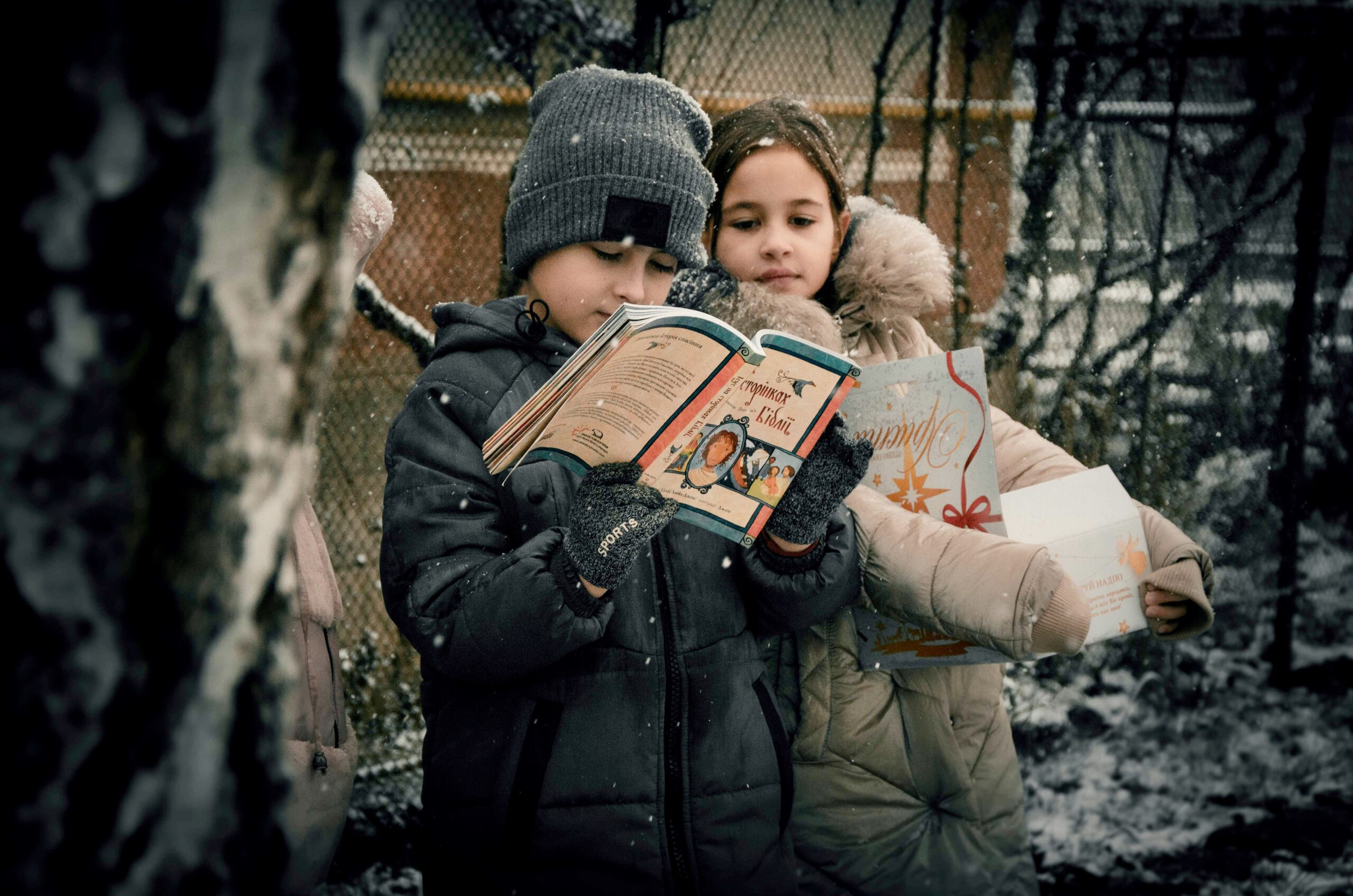 two children reading a bible while standing in the falling snow