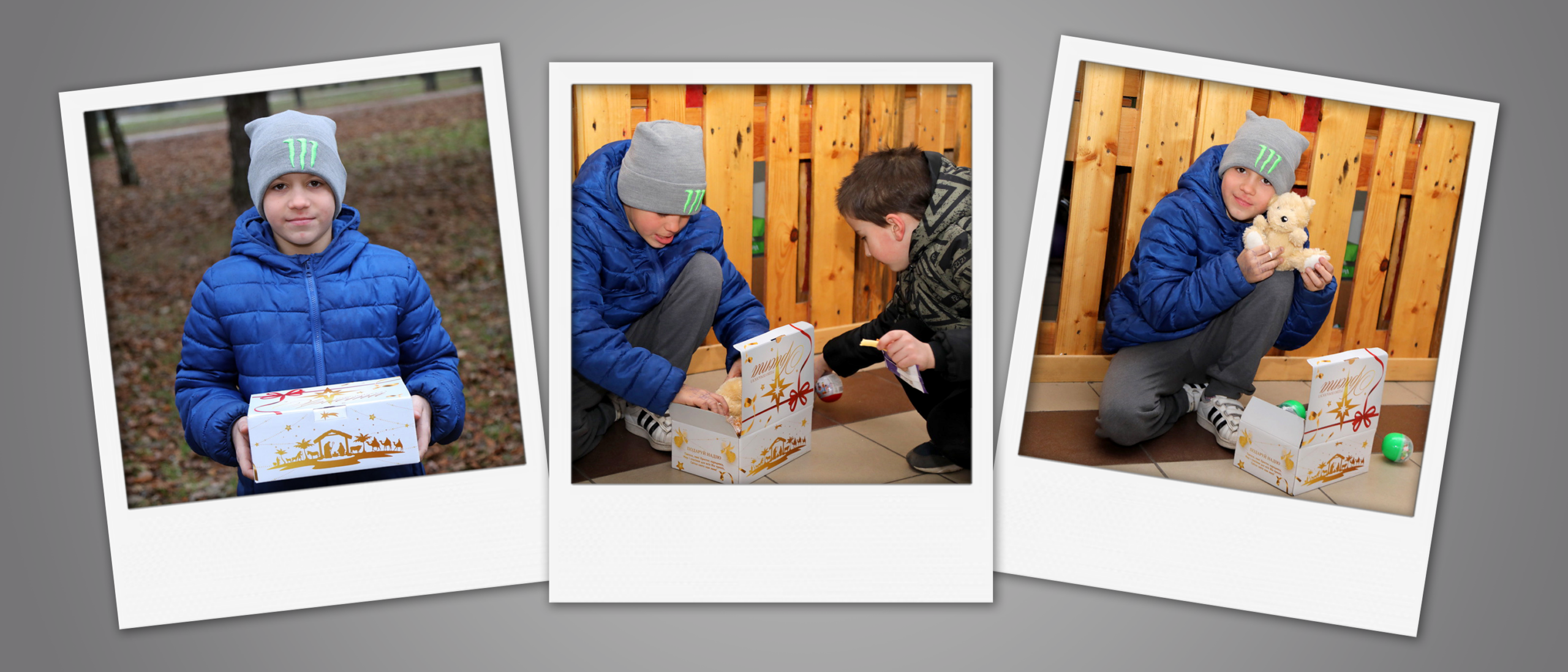 Smiling Ukrainian boy with a beanie and blue jacket crouching, hugging a small teddy bear next to his opened Gift of Hope Christmas box.