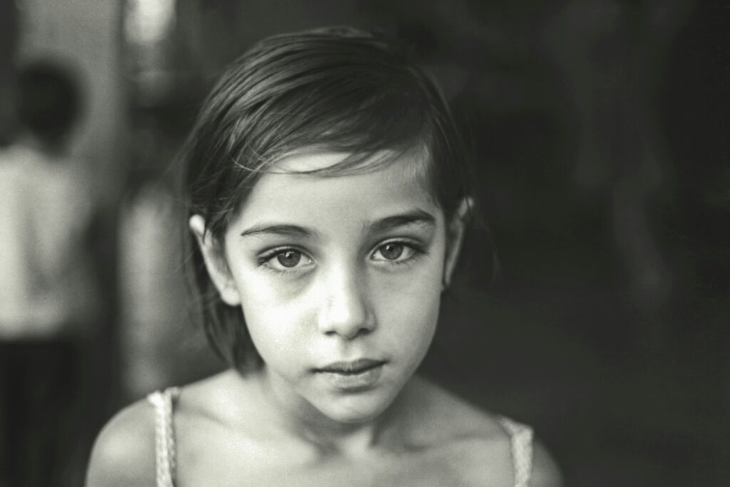 A poignant black and white portrait of a young girl with a solemn expression, representing the emotional impact of being orphaned.