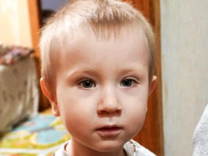 Close-up portrait of a young boy with light brown hair and blue eyes looking directly at the camera with a serious expression.