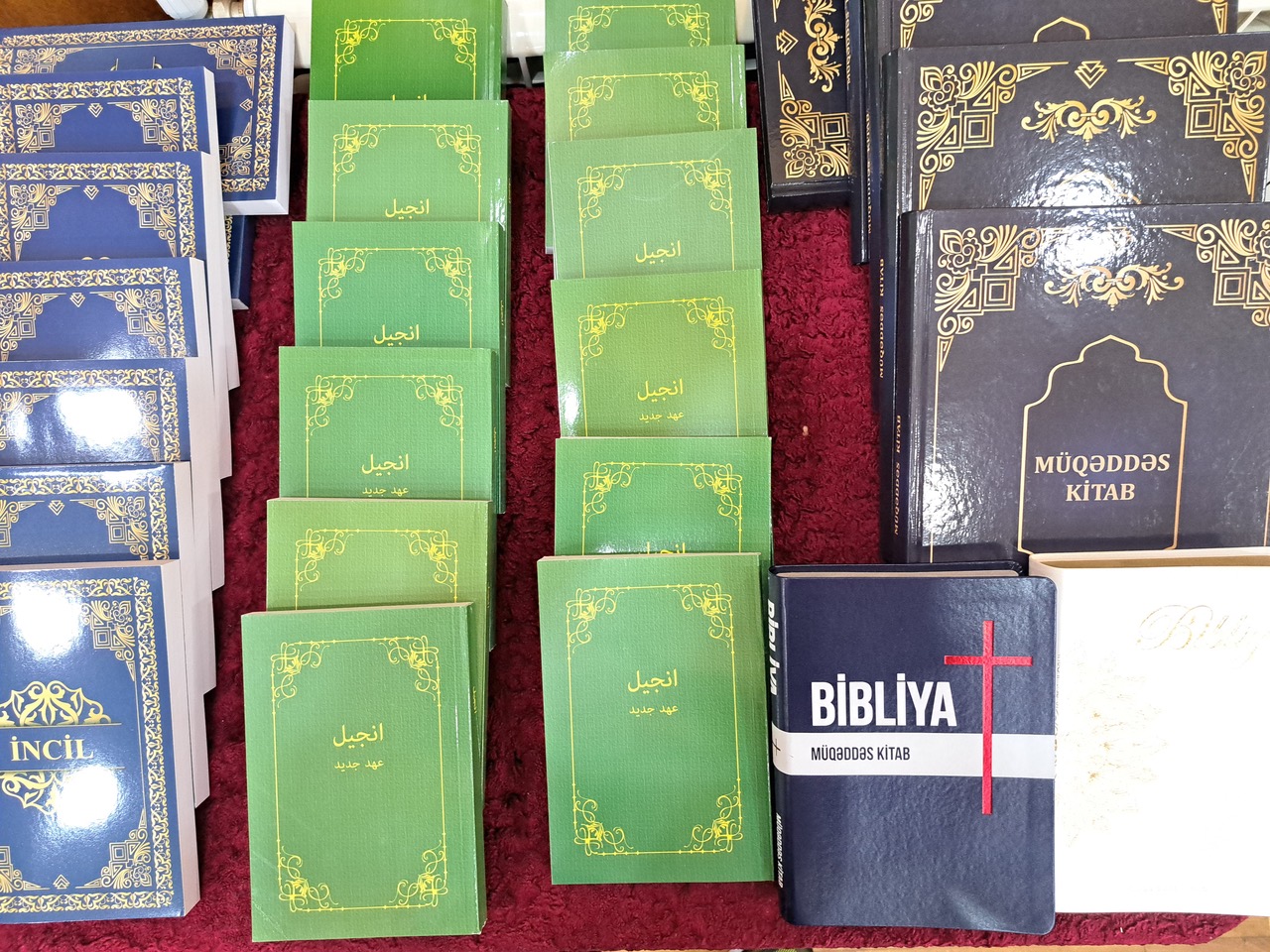 Stacks of Bibles and New Testament books in Azerbaijani and Arabic scripts, including the "Müqəddəs Kitab" and "İncil," displayed for ministry distribution.