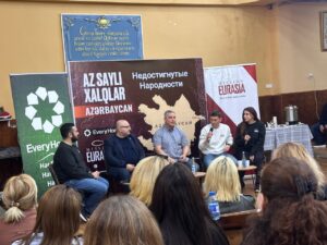 A panel of ministry leaders speaking at a Mission Eurasia event in Azerbaijan, with banners displaying maps of unreached people groups and ministry branding in the background.