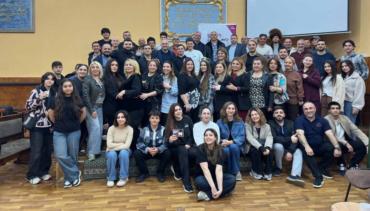 A large group of Mission Eurasia ministry leaders and volunteers posing for a photo during a training event in Azerbaijan, standing in front of ministry banners and a presentation screen.