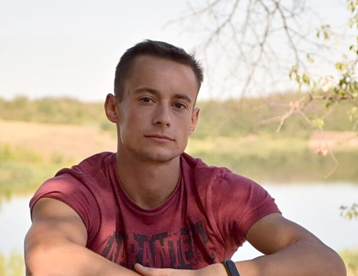 Viktor Maniushkin sitting outside against a natural blurred background of trees and water