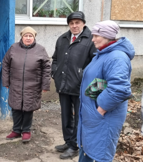Pastor Leonid Skumatov, wearing a dark jacket, hat, and red tie, stands outside with his wife Liubov and daughter Daria in Myrnohrad, Ukraine.
