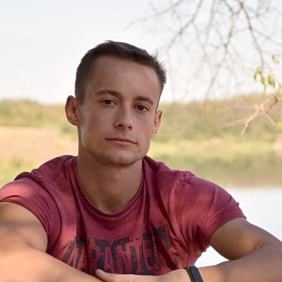 Viktor Maniushkin sitting outside against a natural blurred background of trees and water