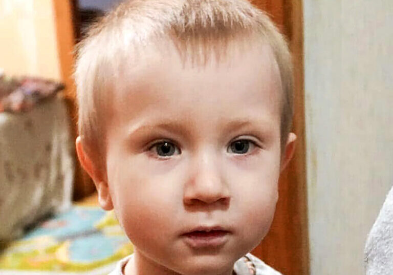 Close-up portrait of a young boy with light brown hair and blue eyes looking directly at the camera with a serious expression.